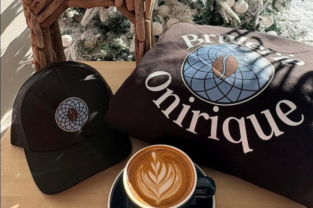 Café au lait dans une tasse posé sur une table en bois accompagné d'une casquette et d'un chandail chaud à l'effigie de la Brûlerie Onirique