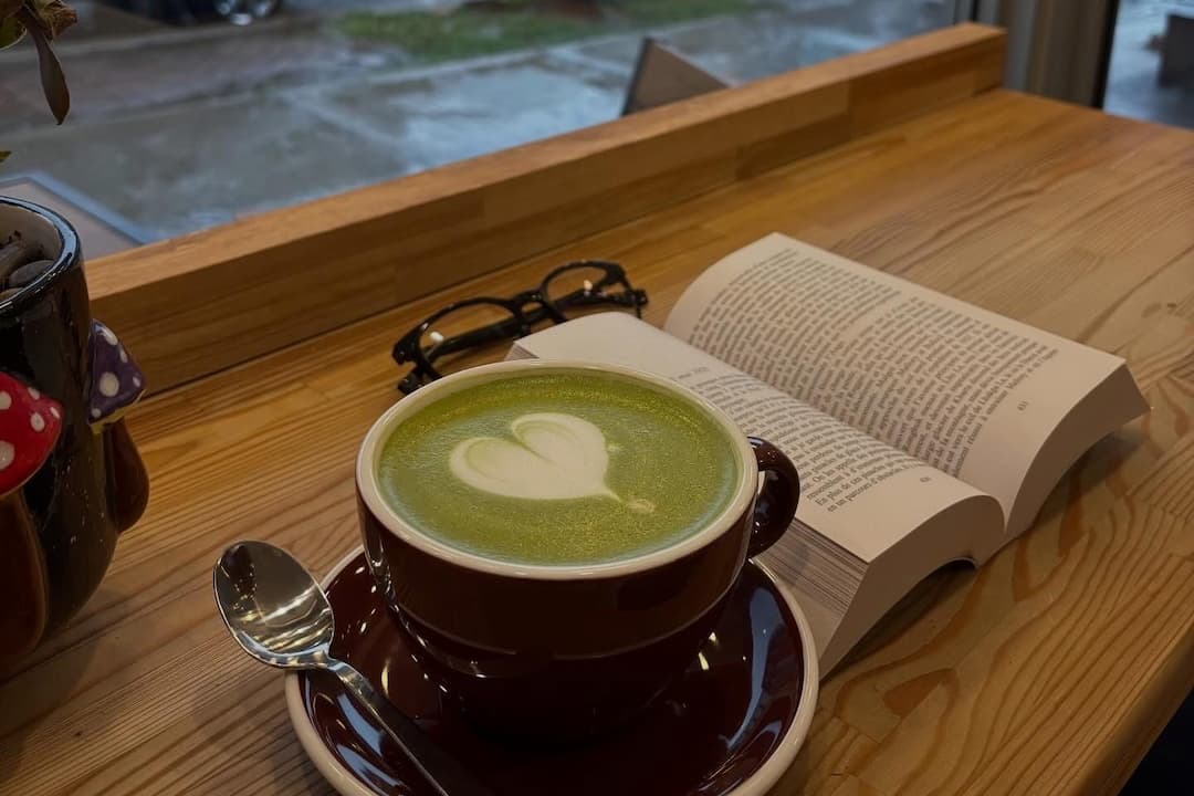 Tasse avec matcha au lait chaud, livre et lunette sur la banquette avec vue sur la rue