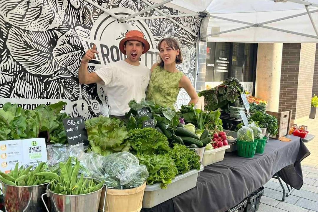 Deux membres de la Coopérative Ferme La Roquette derrière leur kioske de légumes