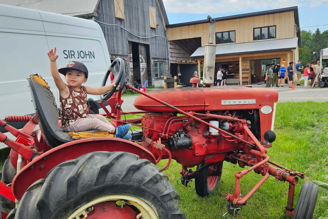 Jeune enfant sur un tracteur rouge à la Coopérative Ferme La Roquette